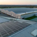 Les panneaux solaires installés sur les toits des bâtiments industriels créent un magnifique bâtiment photovoltaïque, avec en arrière plan, au coucher du soleil, de grands entrepôts et des terres ouvertes, qui illustrent la transition écologique en action.